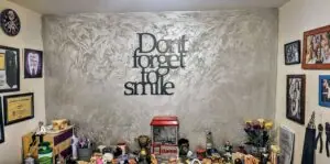 שלט קיר Don't forget to smile מעל שולחן עמוס פסלונים ותעודות
