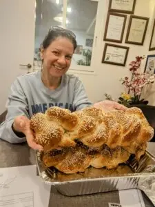אישה מחייכת מציגה חלה קלועה גדולה שהביאה למרפאה במתנה