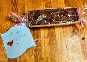 עוגה עטופה בסרט ורוד לצד פתק תודה בכתב יד עם ציור לב וסמיילי